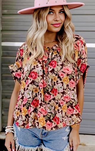 Woman wearing a floral top and denim shorts with a pink hat.