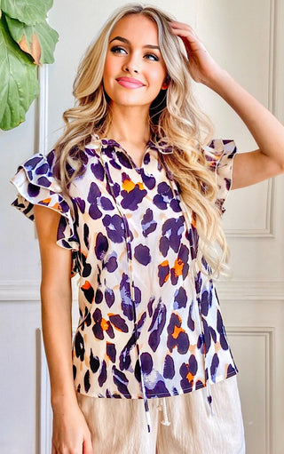 Woman wearing a leopard print top with ruffled sleeves indoors.