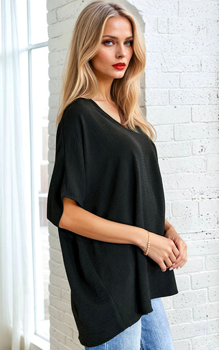 Woman wearing a black oversized top and blue jeans against a white brick wall.