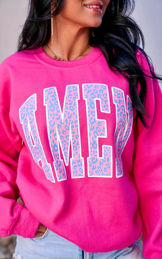 A person wearing a hot pink sweatshirt with 'AMEN' printed in white and leopard print patterns on the letters.