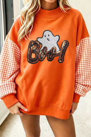 An orange crewneck sweatshirt with a sequined 'Boo!' graphic and a white ghost motif on the front, featuring orange and white gingham checkered sleeves, shown on a model.