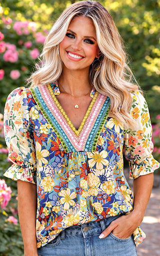 Blonde model wearing a colorful floral V-neck top with multicolor trim, styled with denim shorts outdoors