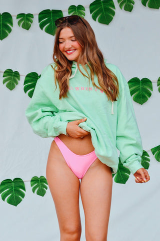 Woman wearing a green hoodie and pink bikini bottom with a leafy background