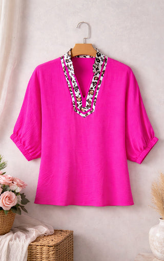 Pink blouse with a leopard neckline on a hanger against a light background