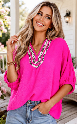 Woman wearing a bright pink top with a leopard print necklace outdoors.