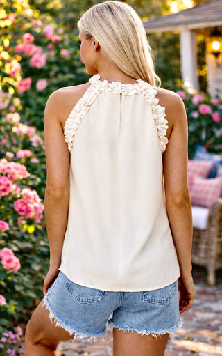 Back view of blonde model wearing Ivory ruffle halter tank top with denim shorts on a bright Southern porch with pink flowers