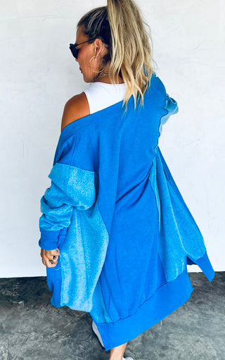 Back view of Woman wearing a blue oversized jacket with a white top underneath against a plain background