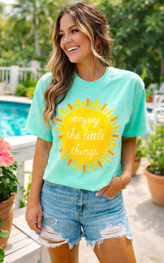 Woman wearing a light green t-shirt with a yellow sun graphic and text, standing outdoors by a pool.
