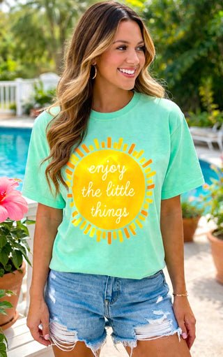 Woman wearing a light green t-shirt with a yellow sun graphic and text, standing by a pool.