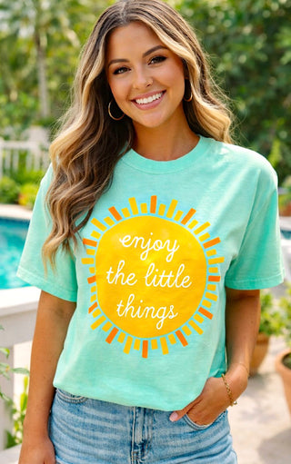 Woman wearing mint green Enjoy the Little Things graphic tee with sunshine print and denim shorts by pool.