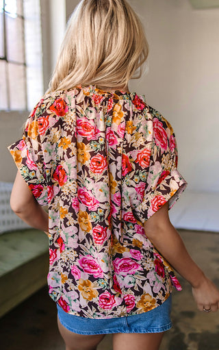 Back view of Blonde woman wearing the Fields of Color Top, a short-sleeve floral blouse with ruffle neckline and tie detail