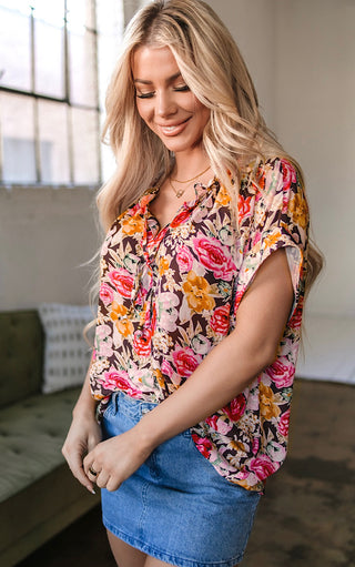 Woman wearing a colorful floral blouse and denim skirt indoors.