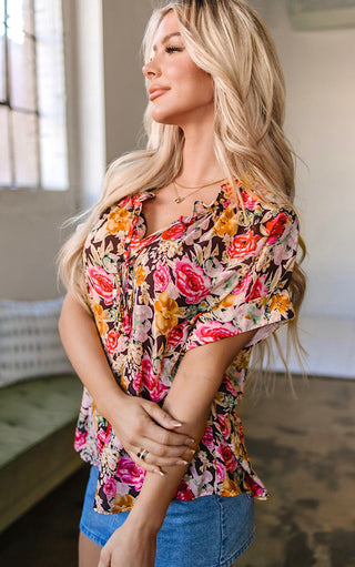 Side view of Blonde woman wearing the Fields of Color Top, a short-sleeve floral blouse with ruffle neckline and tie detail