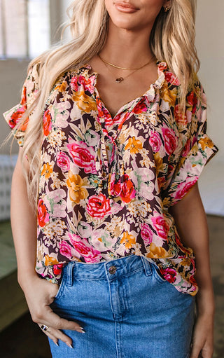 Close up of Blonde woman wearing the Fields of Color Top, a short-sleeve floral blouse with ruffle neckline and tie detail