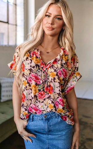 Blonde woman wearing the Fields of Color Top, a short-sleeve floral blouse with ruffle neckline and tie detail