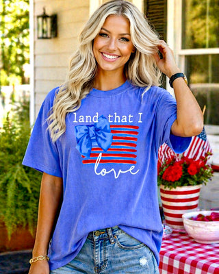 Woman wearing a blue t-shirt with 'land that I love' design, standing outdoors.
