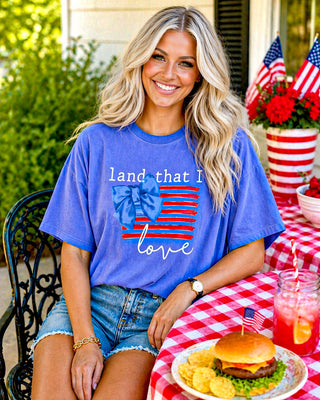 Woman wearing a blue t-shirt with an American flag design, sitting at a table with food and drinks.