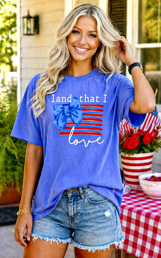 Woman wearing a blue t-shirt with an American flag design and text, standing outdoors.