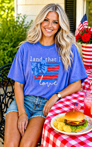 Woman wearing a blue t-shirt with an American flag design, sitting at a table with food and an American flag in the background.