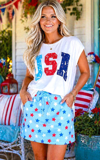 Woman wearing a white 'USA' t-shirt and blue star-patterned skirt in a festive outdoor setting.