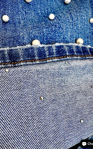 Detail of Blakeley pearl-studded denim fabric showing riveted pearl accents on blue cropped jeans.