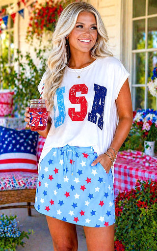 Woman wearing a 'USA' t-shirt and star-patterned skirt outdoors.
