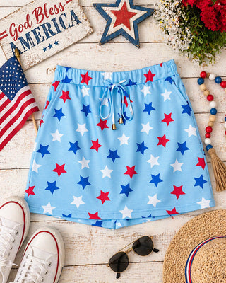Blue shorts with red, white, and blue star pattern on a wooden surface with American flag and 'God Bless America' sign.