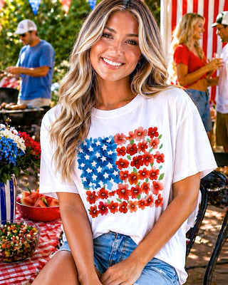 Woman wearing a white t-shirt with an American flag design, sitting outdoors at a casual event.