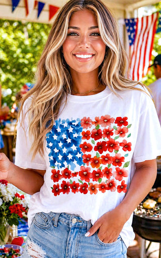 Woman wearing a white t-shirt with a colorful American flag design, standing outdoors with flags in the background.