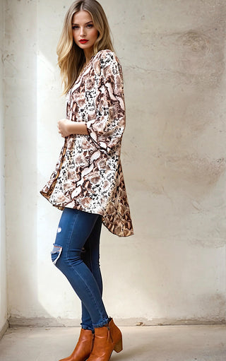 Model wearing a snakeskin print kimono cardigan over a white tank top with blue jeans and brown boots. 