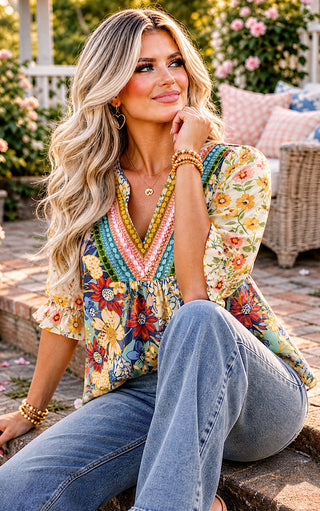 Woman wearing a colorful floral blouse and jeans sitting outdoors.