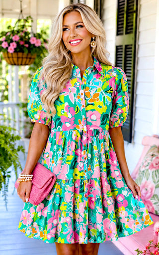  Woman wearing a pink and turquoise floral puff sleeve dress while holding a pink clutch on a cottage-style porch.