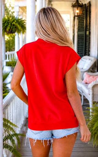 Back view of red top with cap sleeves modeled on a blonde woman outdoors on a Southern porch.