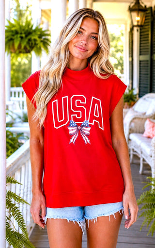 Woman modeling a patriotic red USA graphic mock neck top with cap sleeves and distressed denim shorts.