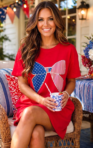 Woman in a red dress with a patriotic design, holding a drink, sitting outdoors.