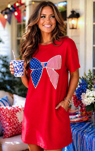 Woman in a red dress with a large blue and white bow design, holding a drink, outdoors.