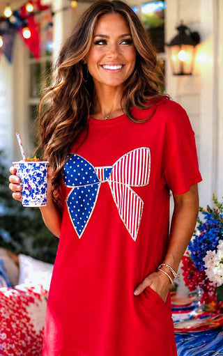 Woman wearing a red Americana dress with a large bow design, holding a cup with a straw.