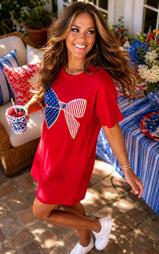 Woman in a red dress with a large American flag bow design, standing outdoors on a patio.