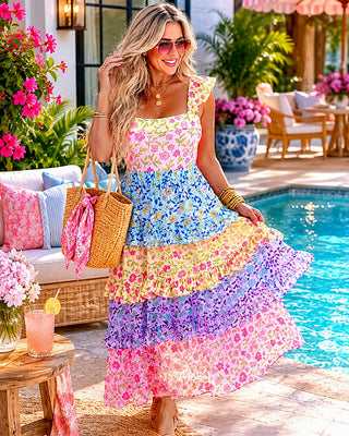 Woman in a colorful floral dress by a poolside with flowers and outdoor furniture.