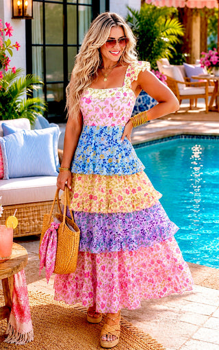 Blonde model posing beside a turquoise pool in a pink floral swimsuit with removable padding and matching colorful cover-up skirt.