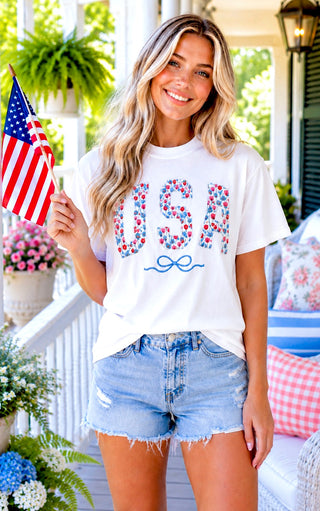 Woman wearing a 'USA' graphic t-shirt on a porch with an American flag