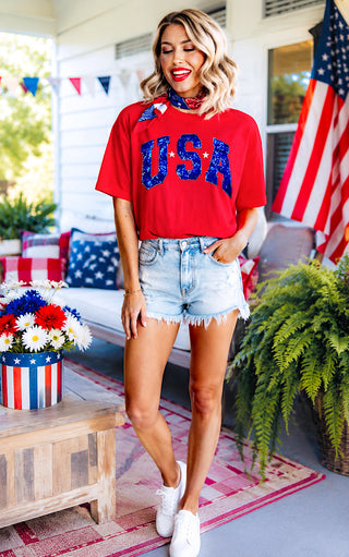 Woman wearing a red 'USA' shirt on a decorated porch.