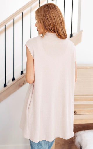 Woman wearing a light cream sleeveless open-front cardigan, showing draped fit from the back.