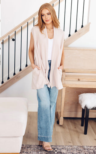 Woman modeling cream sleeveless cardigan with pockets, layered over a white top and wide-leg denim.
