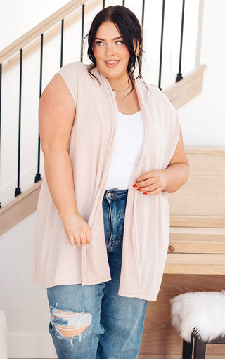Plus size Woman modeling cream sleeveless cardigan with open front and pockets, styled over casual denim.
