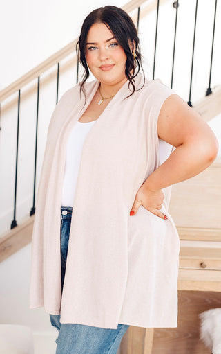 Plus size Woman wearing a beige cardigan over a white top and blue jeans, standing indoors.
