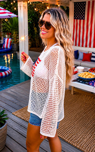 Woman in a white mesh cover-up with red and blue accents by a poolside with American flag decorations.