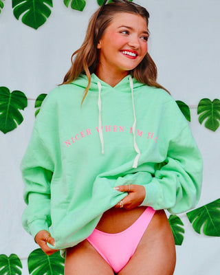 Woman wearing a light green hoodie with text and pink bikini against a leafy background
