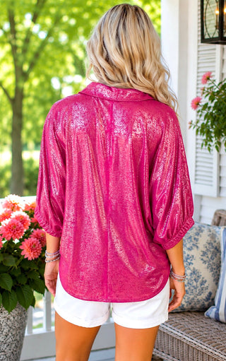 Back view of a Woman wearing a bright pink shirt and white shorts standing outdoors with greenery and a bench in the background.