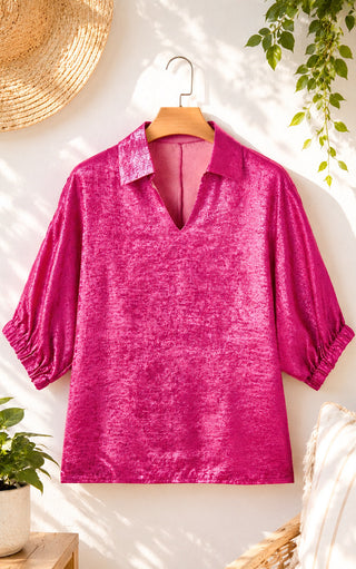 Pink blouse on a hanger against a white wall with plants and decor.